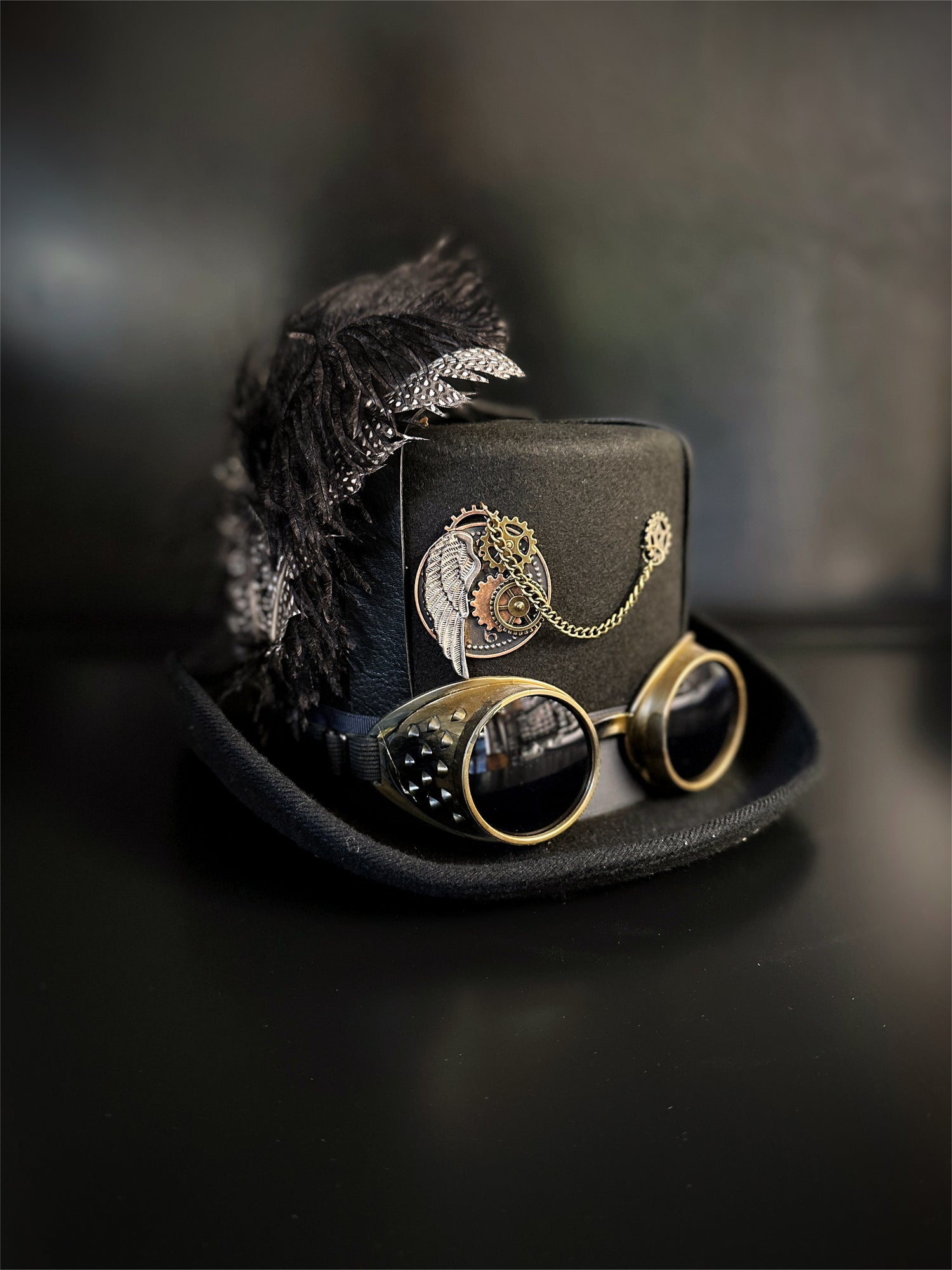 Black steampunk hat with feathers, steampunk motifs, and gold goggles.