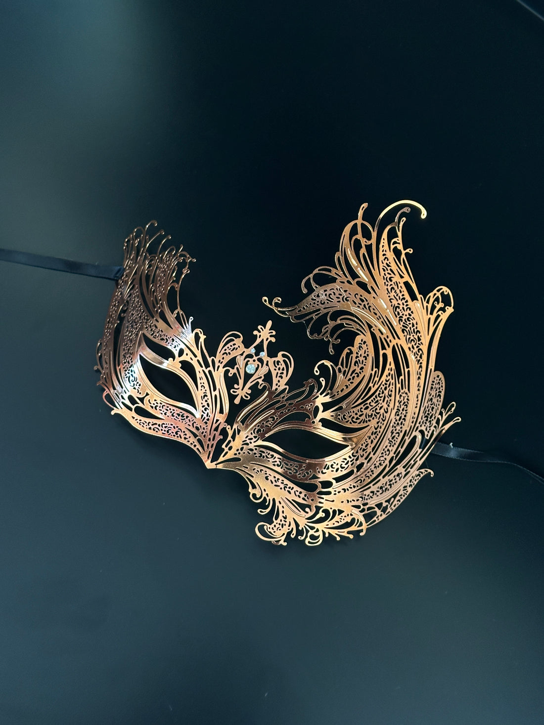 Elegant rose gold masquerade mask inspired by a swan’s wings, with intricate filigree and metallic shine.