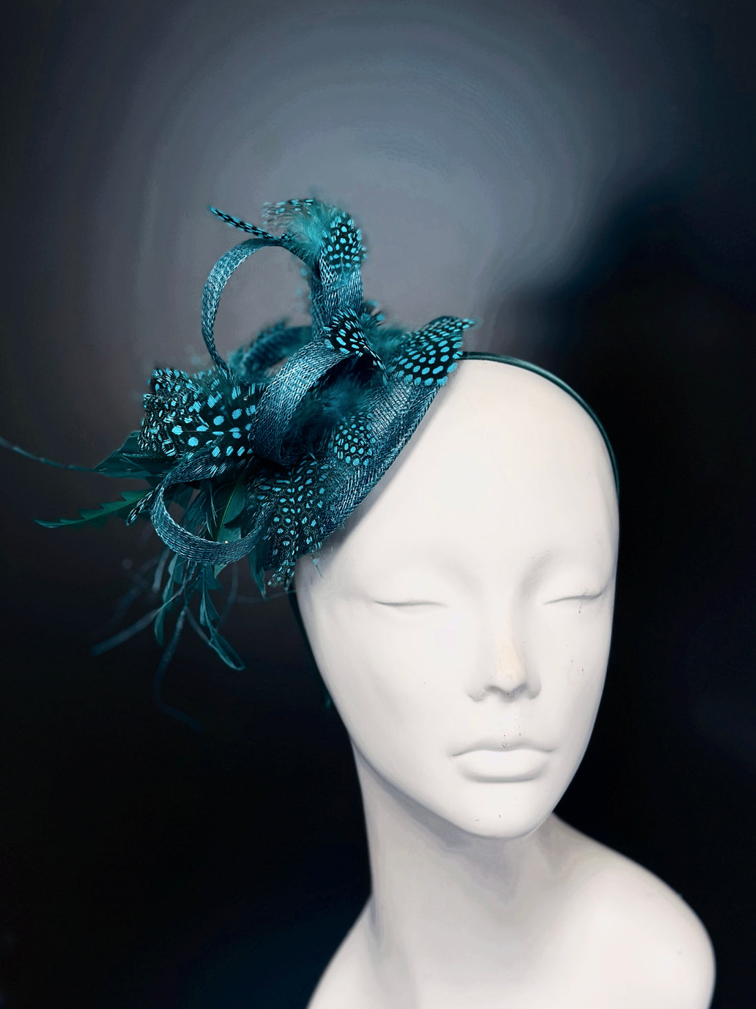 Teal feather fascinator hat with spotted accents, elegant headpiece for weddings and races.