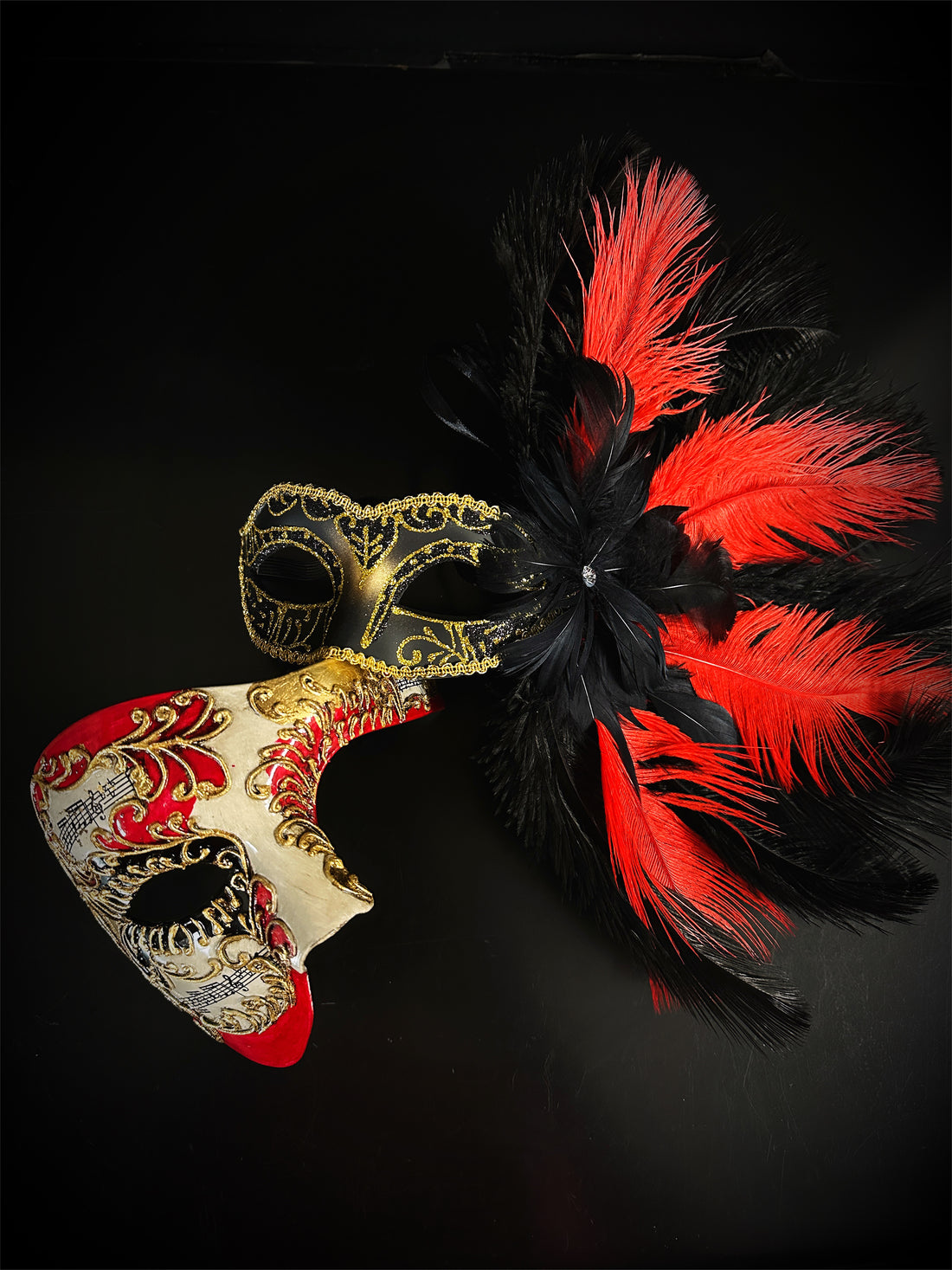 Red and black feather Venetian masquerade mask with gold scrollwork and music note accents.