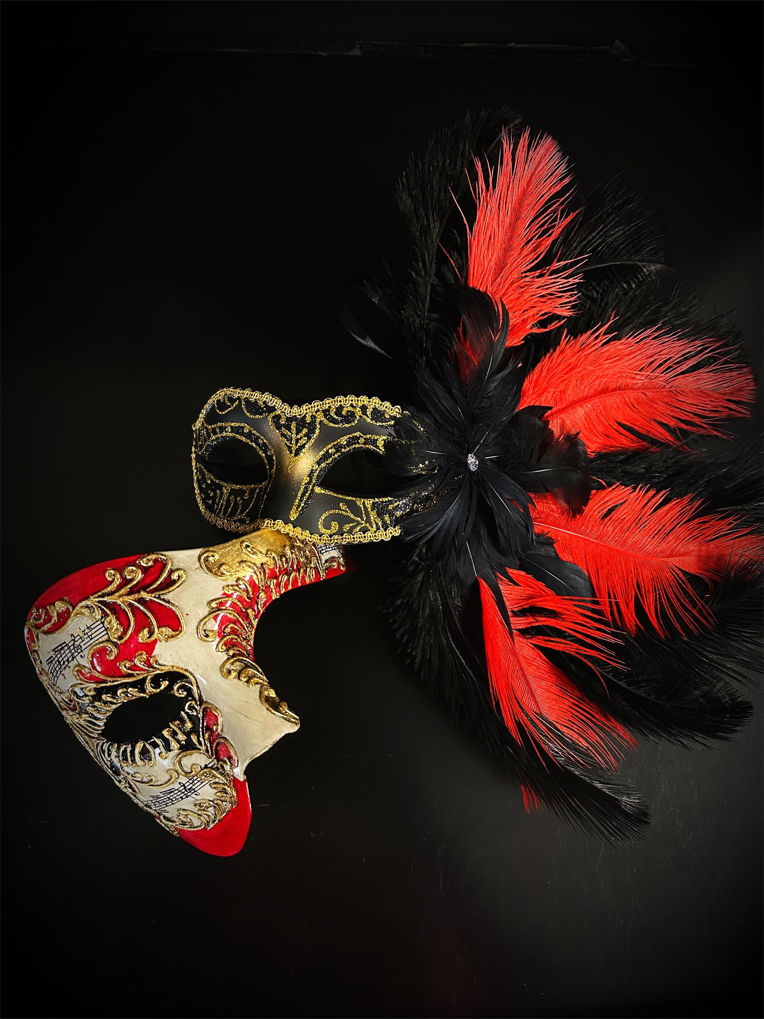 Red and black feather Venetian masquerade mask with gold scrollwork and music note accents.
