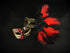Venetian masquerade mask with red and black feathers, gold scrollwork, and music note accents.