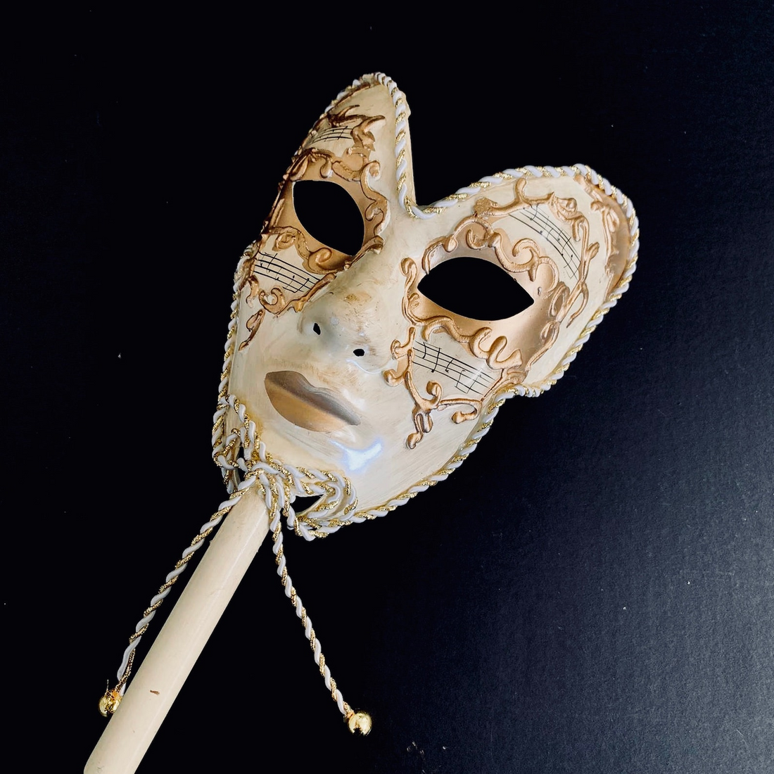 Venetian Volto masquerade mask on stick in ivory and gold with music note design.