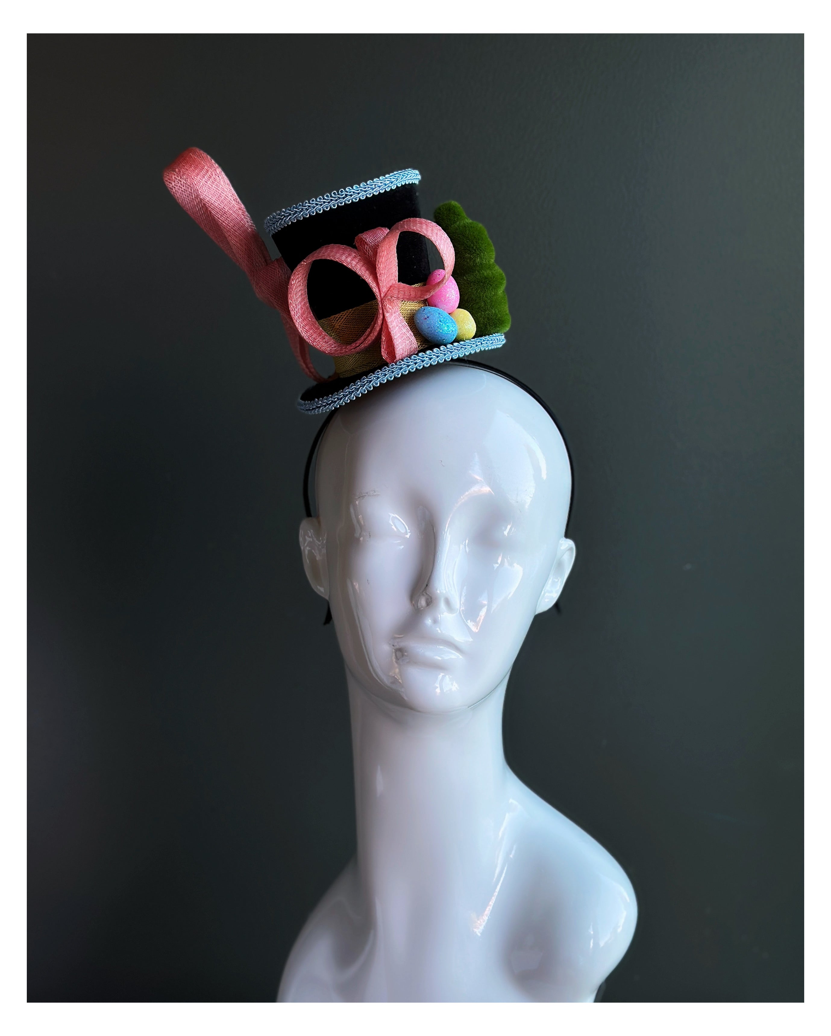 Whimsical mini top hat fascinator for women with a light blue trim, pink sinmay design and eater egg decorations 