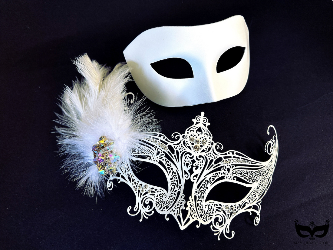 White couples masquerade mask set with matte men’s mask and ornate women’s filigree mask featuring feathers, rhinestones, and crystal cluster.