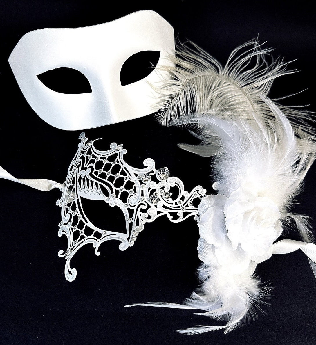Elegant white Venetian couples masquerade masks featuring a simple satin mask for men and a lace mask with feathers and floral accents for women, perfect for weddings and formal events.
