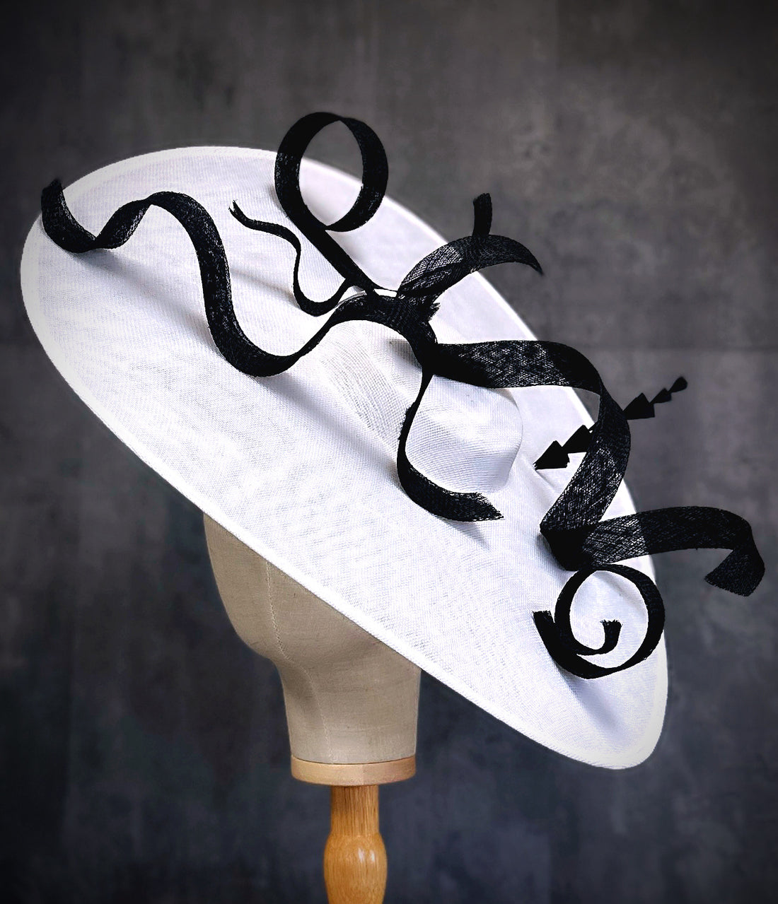 Dramatic wide-brim white fascinator hat with bold black ribbon swirls, couture derby hat for weddings, races, and elegant events.
