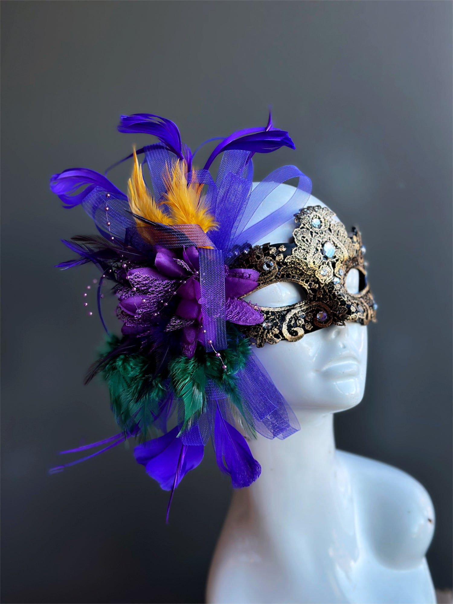 Womens masquerade mask in gold with green, purple, and gold feathers.