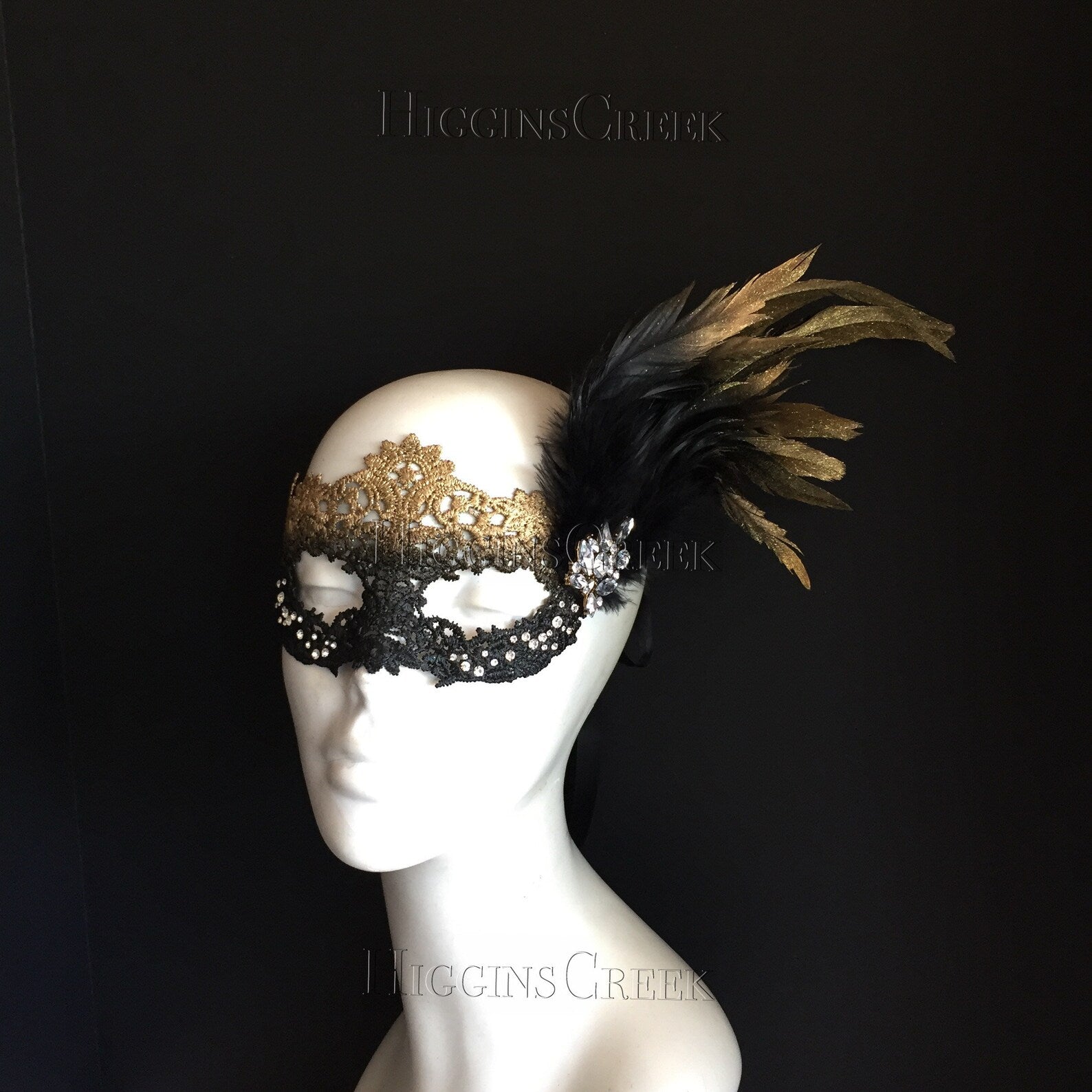 Womens masquerade mask in a gold/black ombre with clear rhinestones, golden feathers, and a crystal brooch.