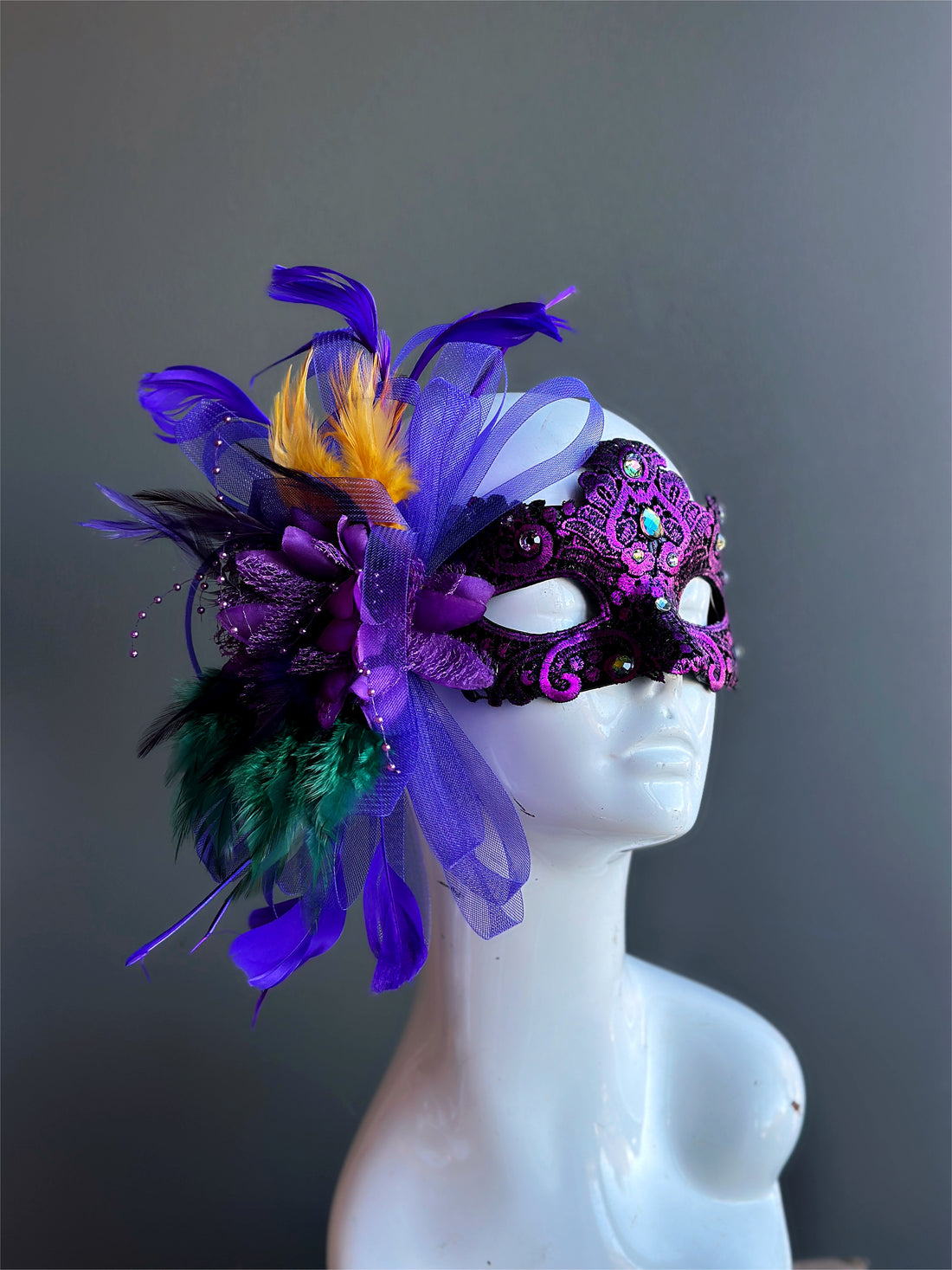 Womens purple masquerade mask with green purple and gold feathers for mardi gras.