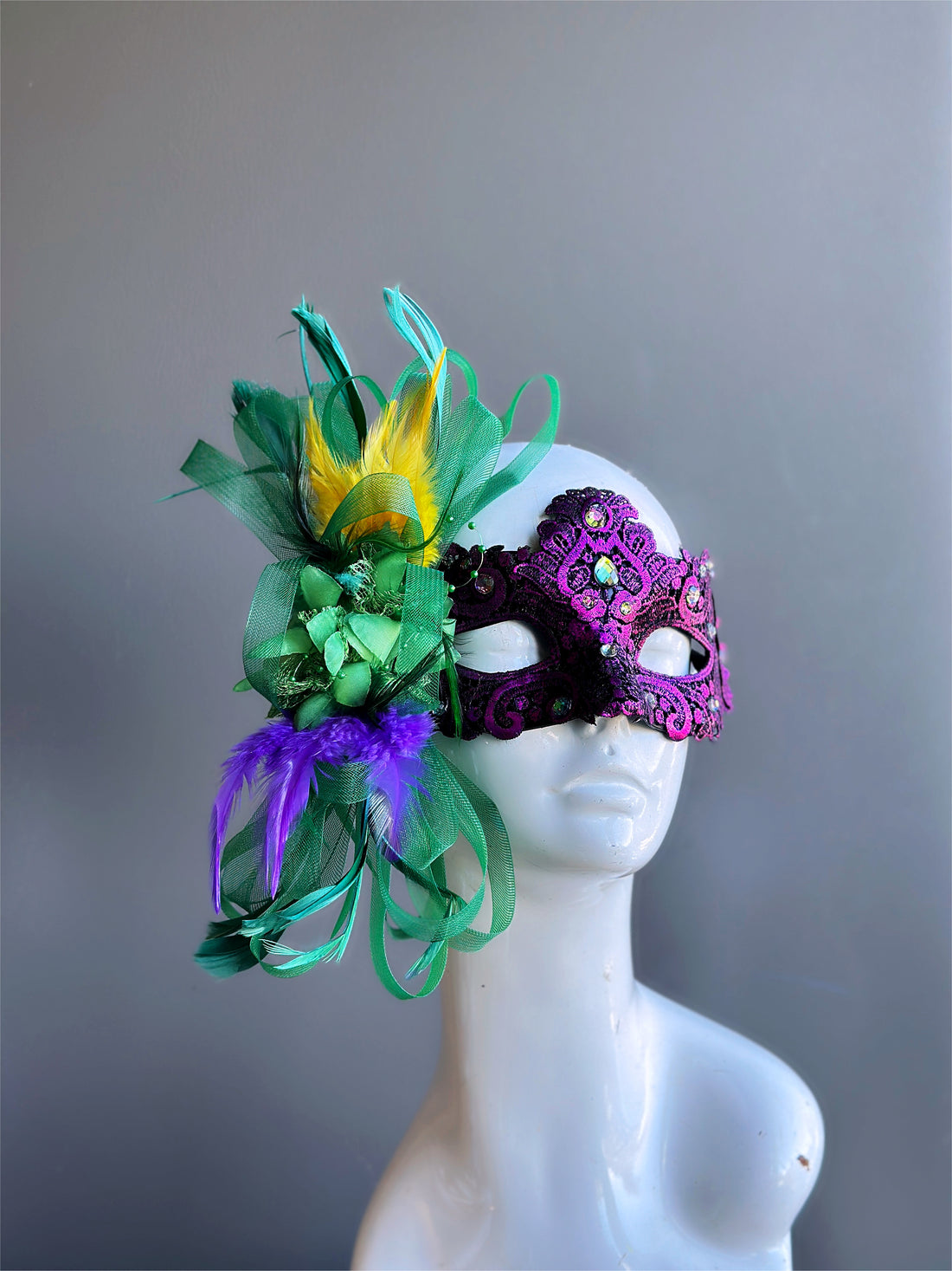 Womens masquerade mask with a purple base, green yellow and purple feathers.