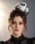 Woodland Owl Nest Fascinator featuring a fluffy white and gray owl, two pastel green speckled eggs, brown twig nest, cream flowers, and black headband.