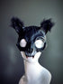 Black cat mask with furry ears, sculpted details, and small fangs, perfect for Halloween and gothic masquerade events.

