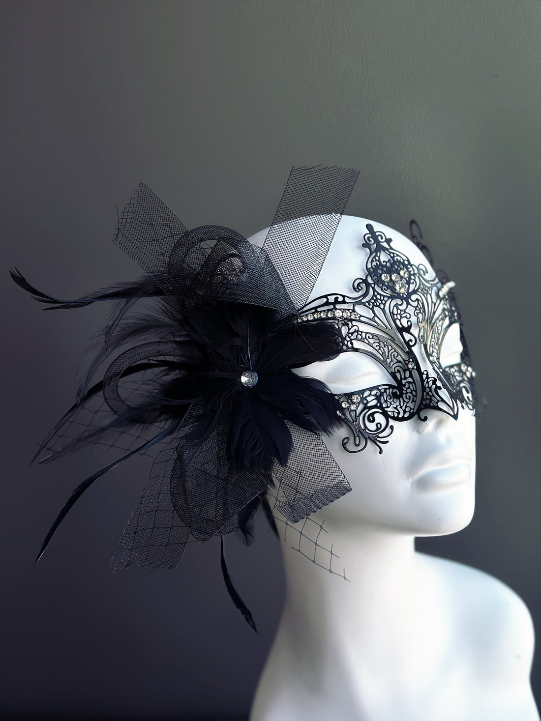 Black masquerade mask with feathers, rhinestones, and black mesh details