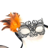 Elegant black filigree masquerade mask with bright orange feathers and rhinestone details.