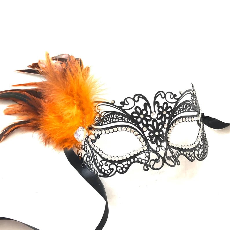 Elegant black filigree masquerade mask with bright orange feathers and rhinestone details.