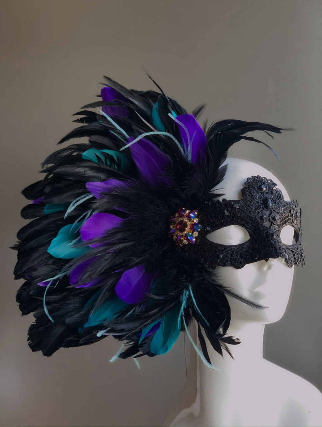 Black lace masquerade mask with blue, purple and black feathers and green highlights for women.