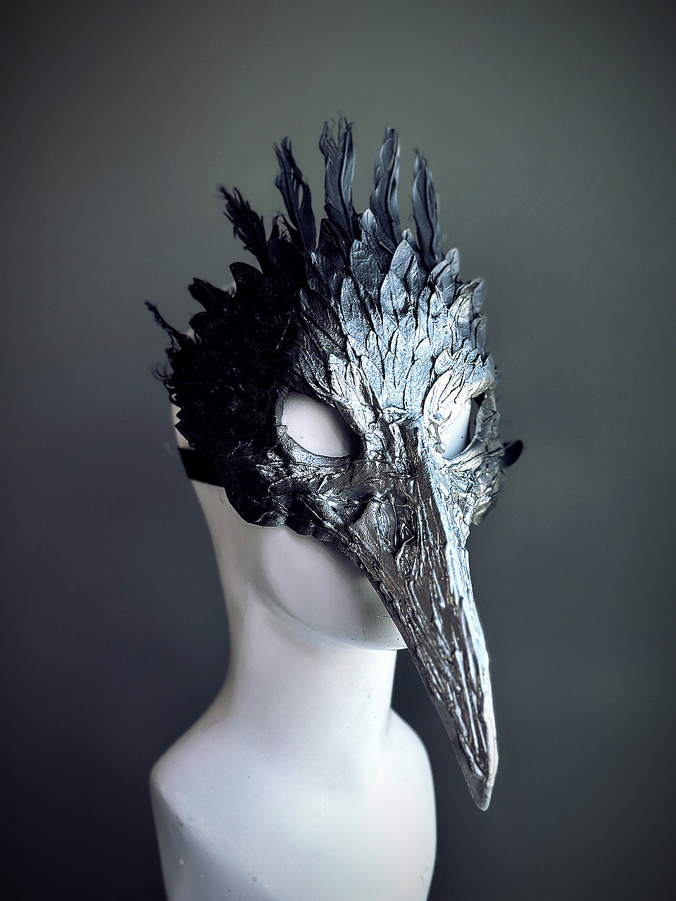 Black and silver bird mask featuring sculpted feather details and a long beak, ideal for masquerades, fantasy events, and theatrical performances.

