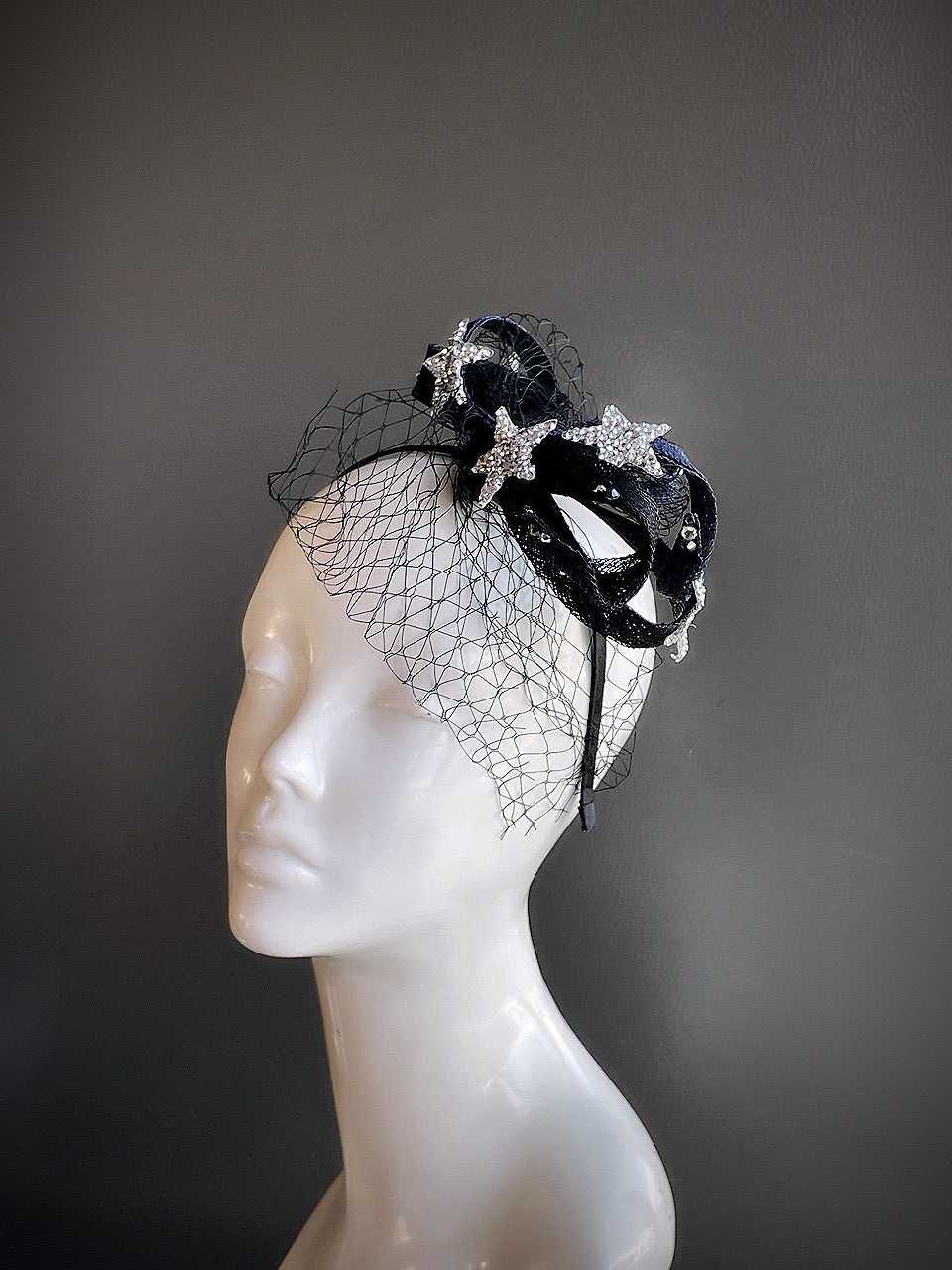 Black fascinator with rhinestone stars and a delicate veil displayed on a mannequin head.