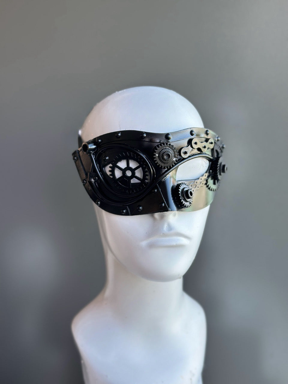 Men’s black steampunk mask with metallic gear accents and an industrial design, displayed on a mannequin.

