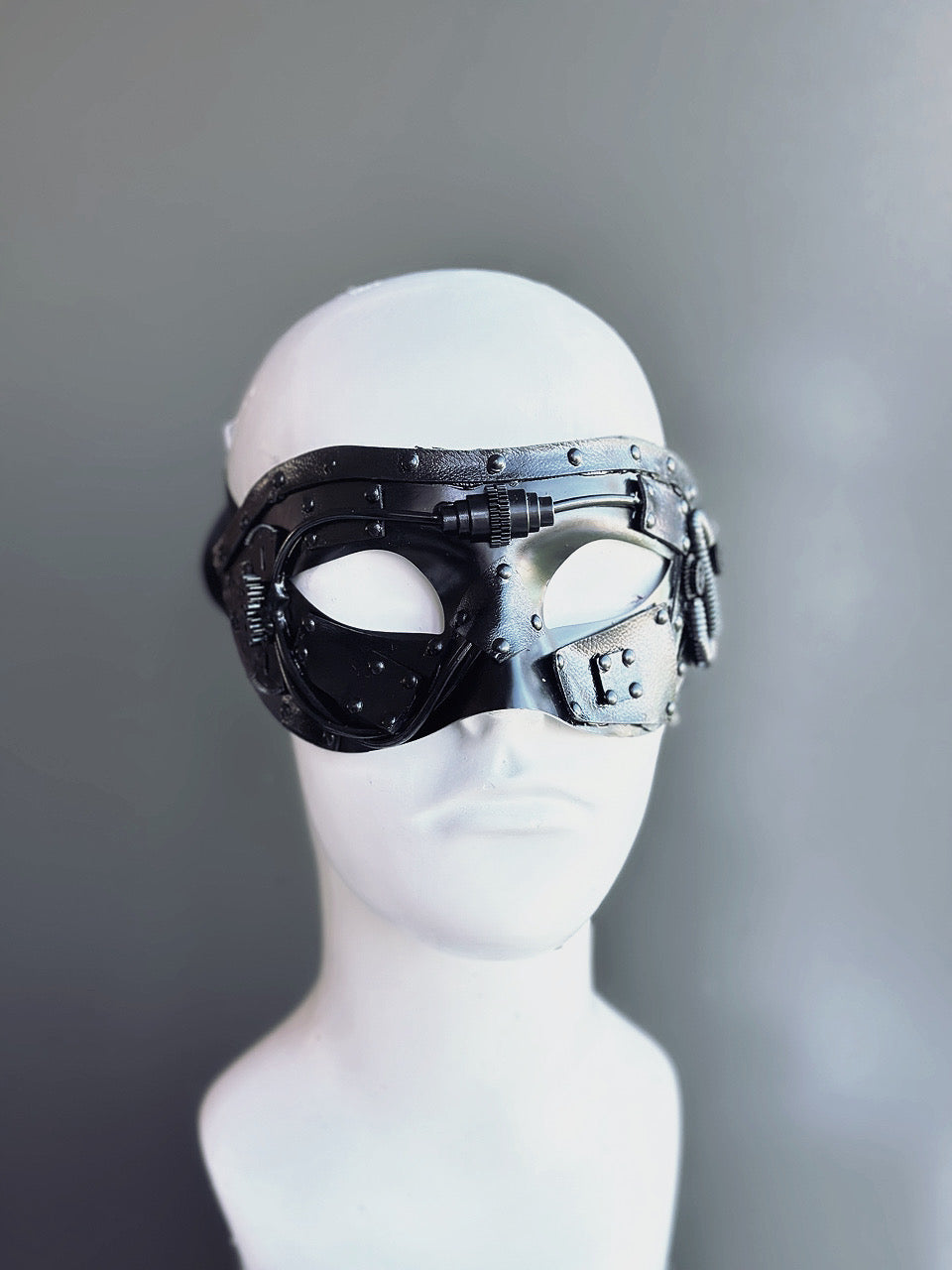 Men’s black steampunk masquerade mask featuring mechanical accents and an industrial design, displayed on a mannequin.

