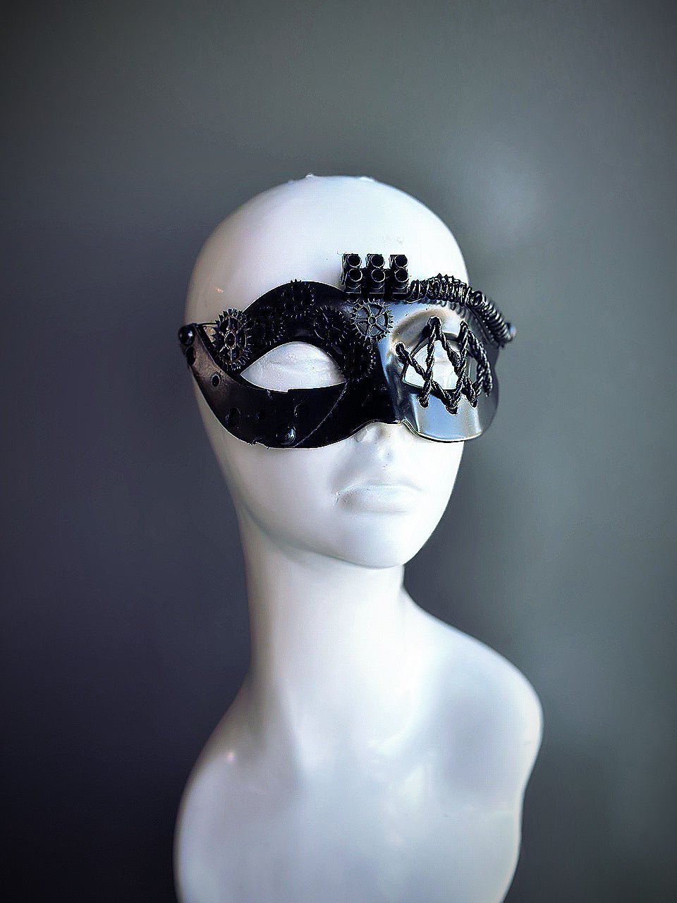 Black steampunk masquerade mask for women with intricate gear details and industrial-inspired design, displayed on a mannequin head.