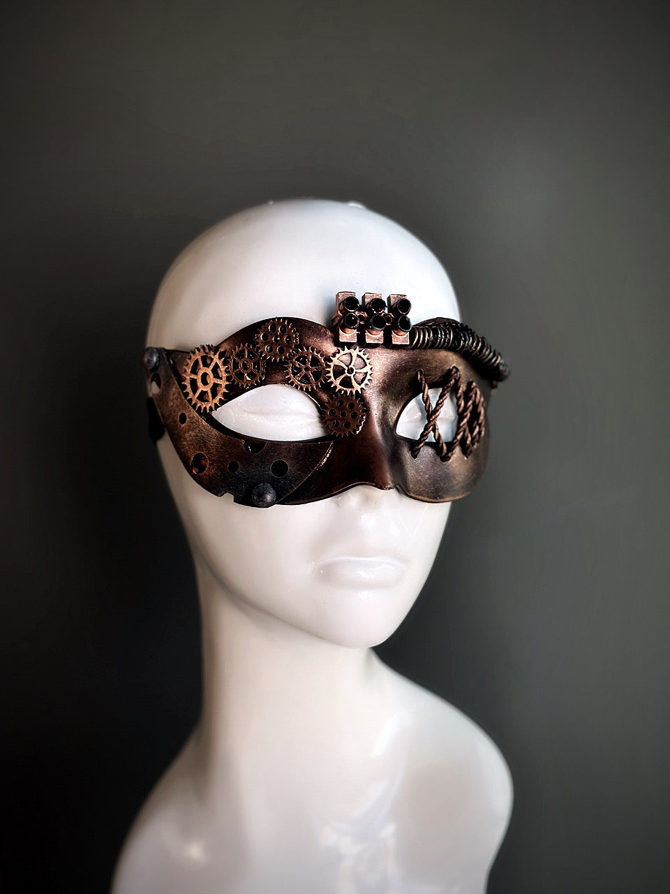 Bronze steampunk masquerade mask for women with intricate gear detailing and metallic accents, displayed on a mannequin head.

