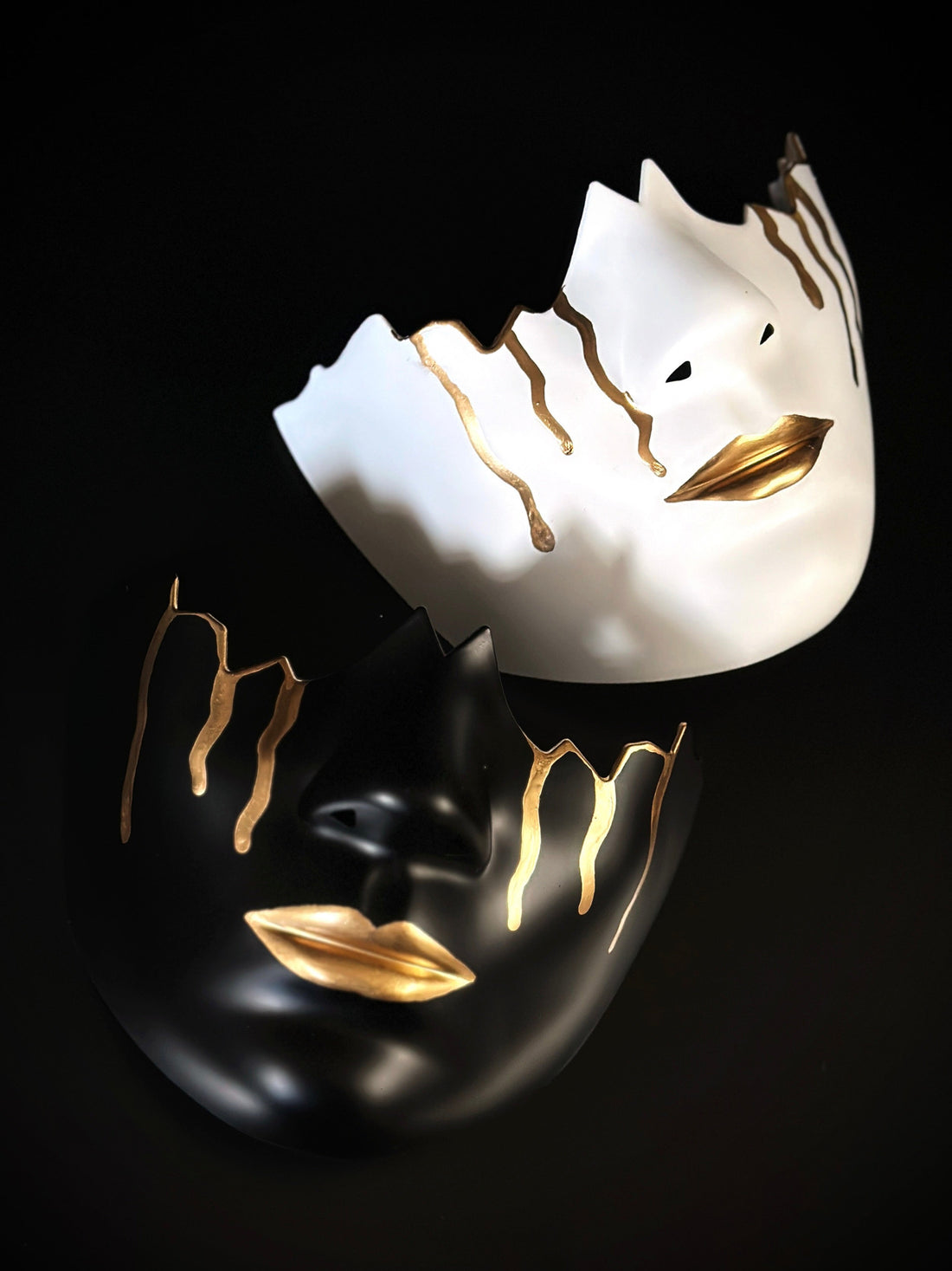 A matching set of black and white cracked mouthguard masks both with gold lips and gold tear drops. 