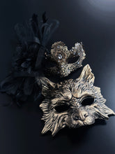 Womens gold lace and gem masquerade mask with black feathers, paired with a gold and black wolf masquerade mask.