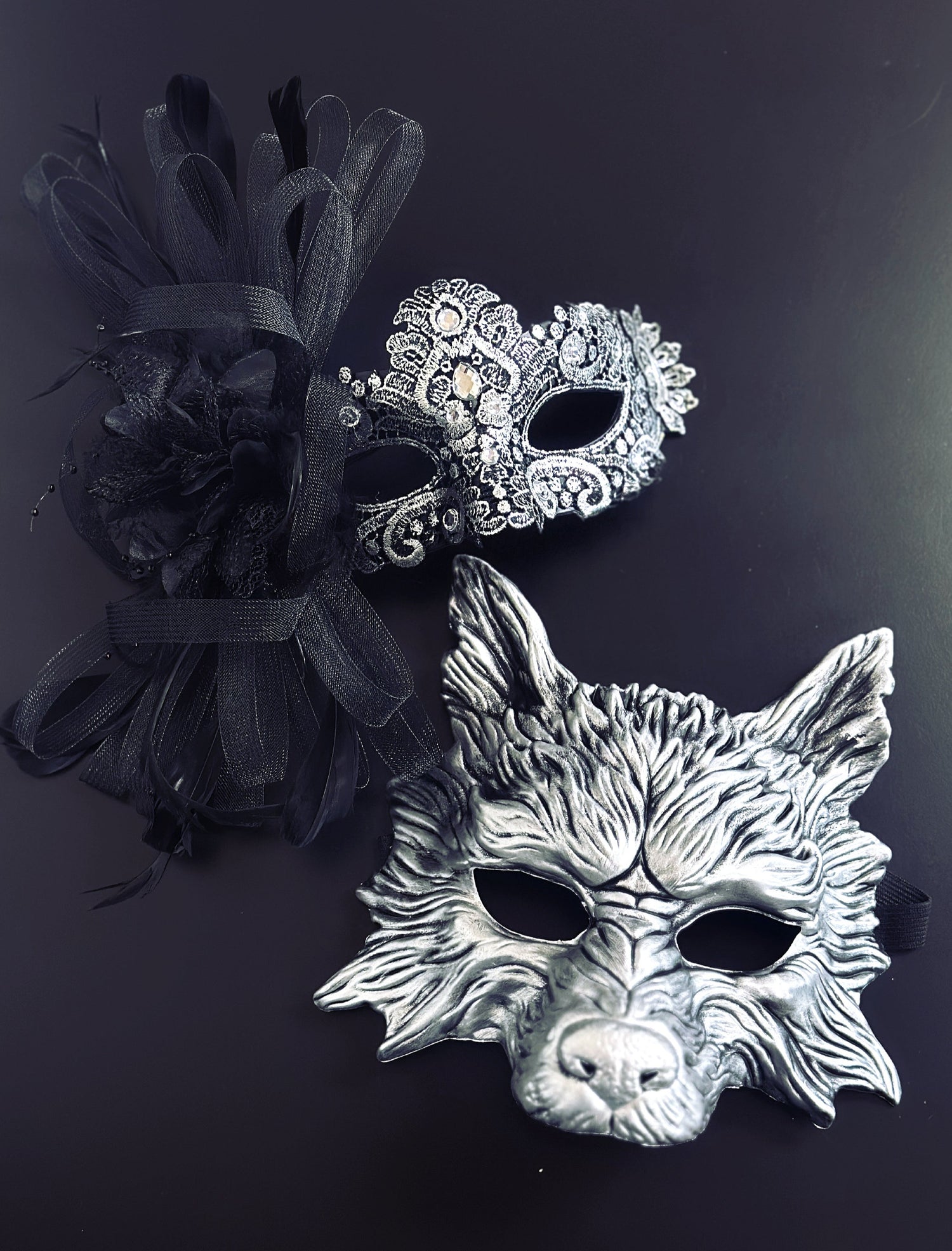 Silver lace womens masquerade mask with black feathers, paired with a black silver men&