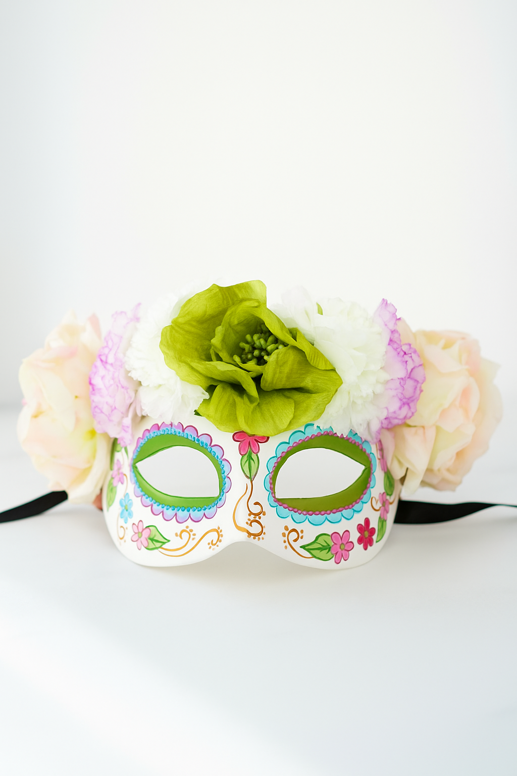 Sugar skull mask with pastel flower crown in green, pink, and cream for Dia de los Muertos.