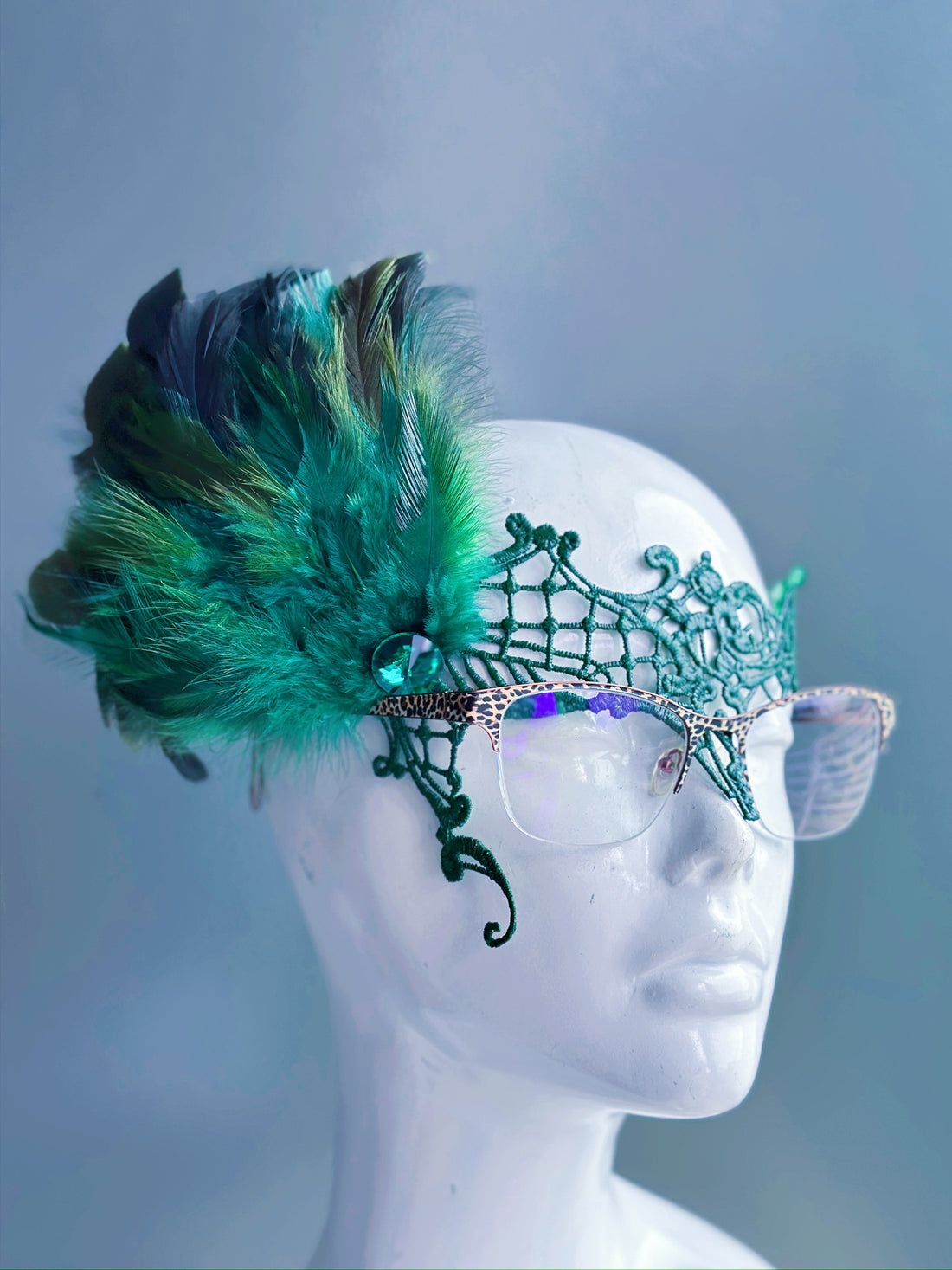 Emerald green lace eyeglass mask with filigree, feathers, and a jewel, designed for eyeglass wearers.