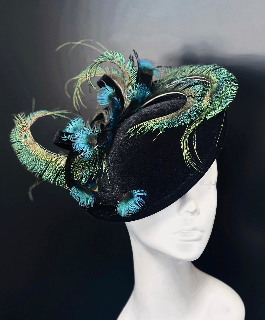Black velvet fascinator hat base on a clip and headband with swirling peacock feathers.