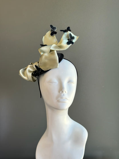 Champagne colored satin ribbon fascinator hat with black butterfly accents for weddings and cocktail events.