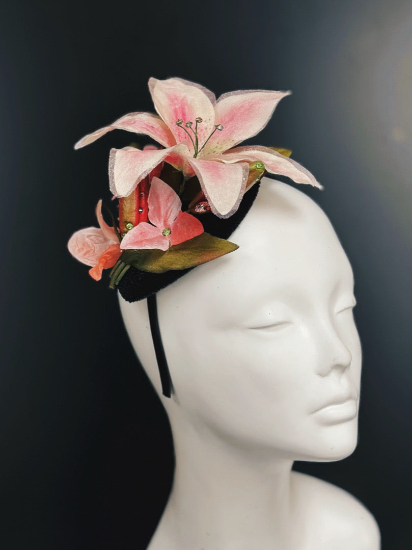 Black base fascinator hat decorated with pink lily flowers and rhinestone accents.