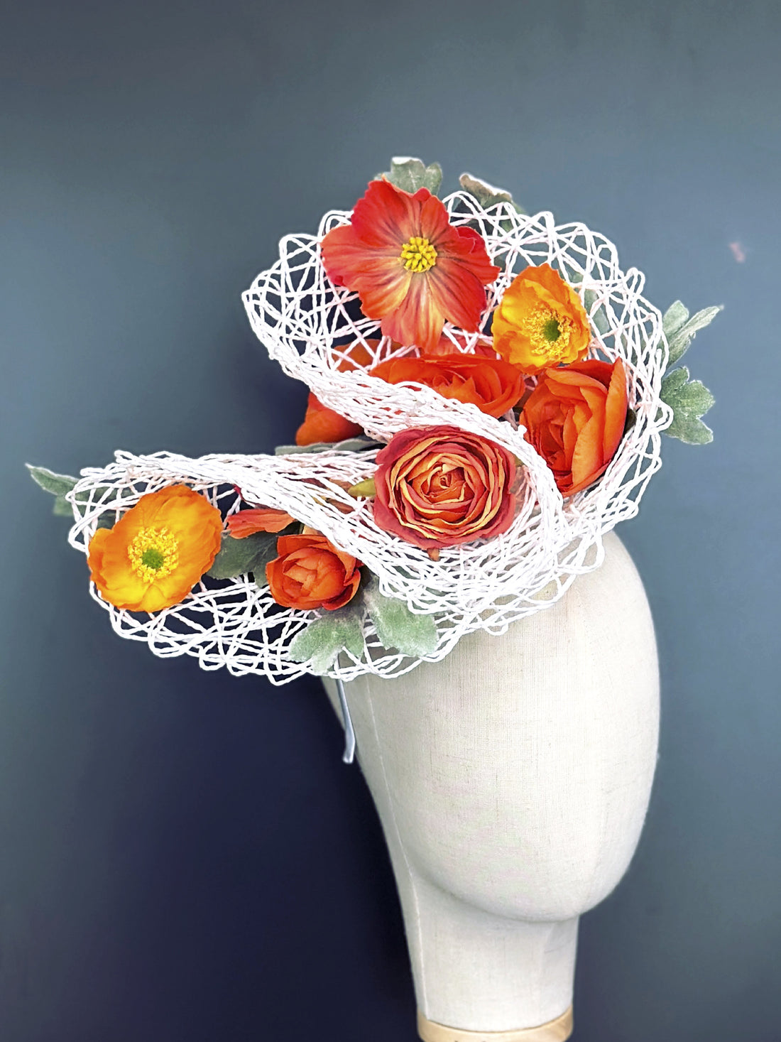 White fascinator hat base with florals in shades of orange.