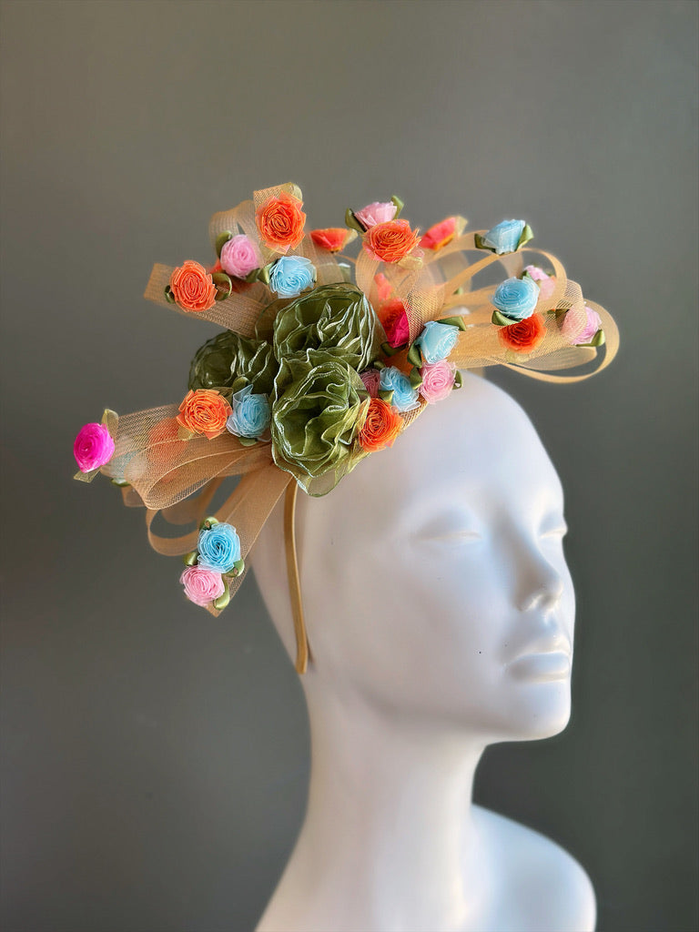 Pastel floral sinamay fascinator with ribbon roses and mesh loops for derby and wedding occasions.