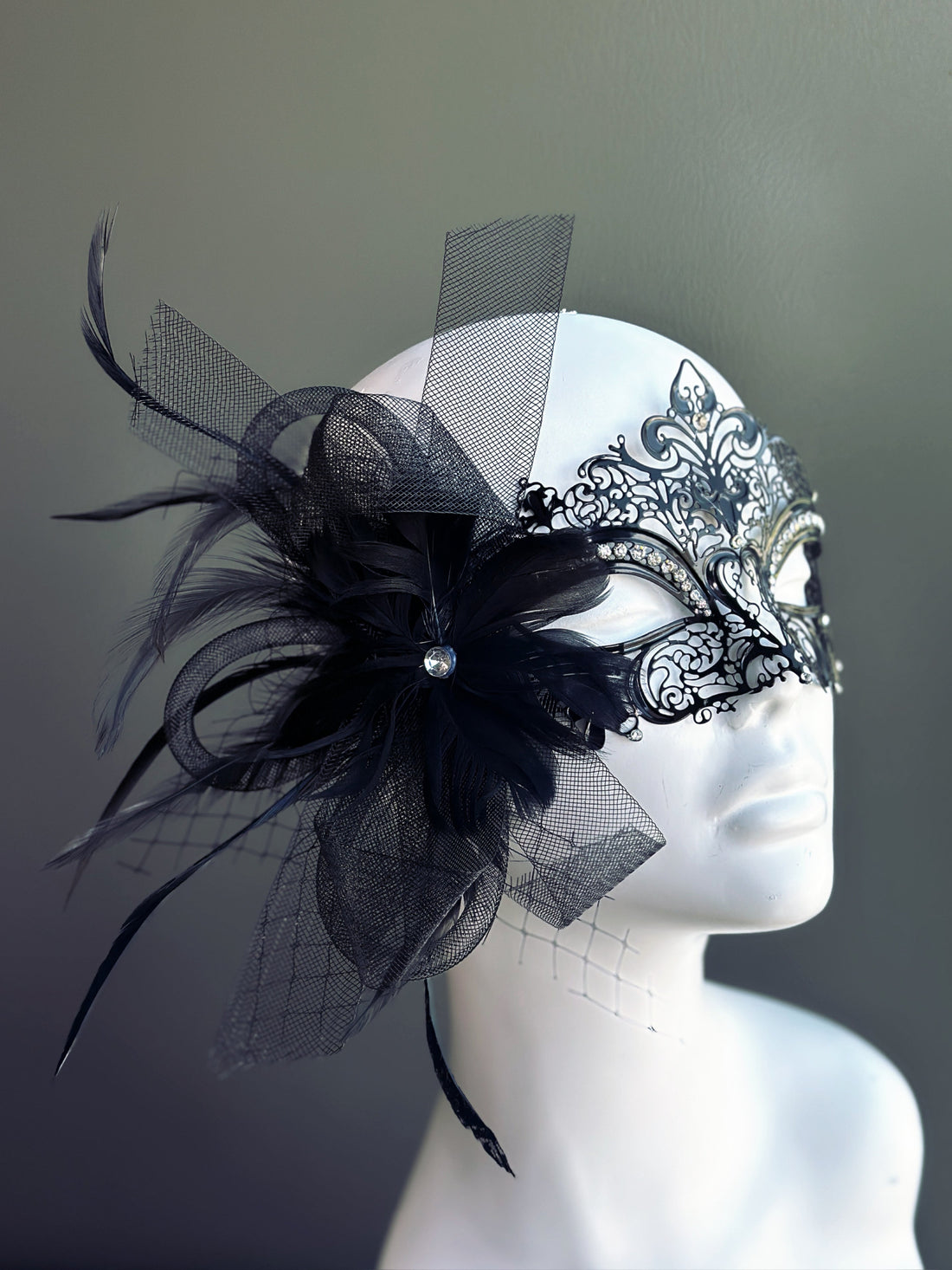 Black metal masquerade mask with feathers, rhinestones, and black mesh detailing