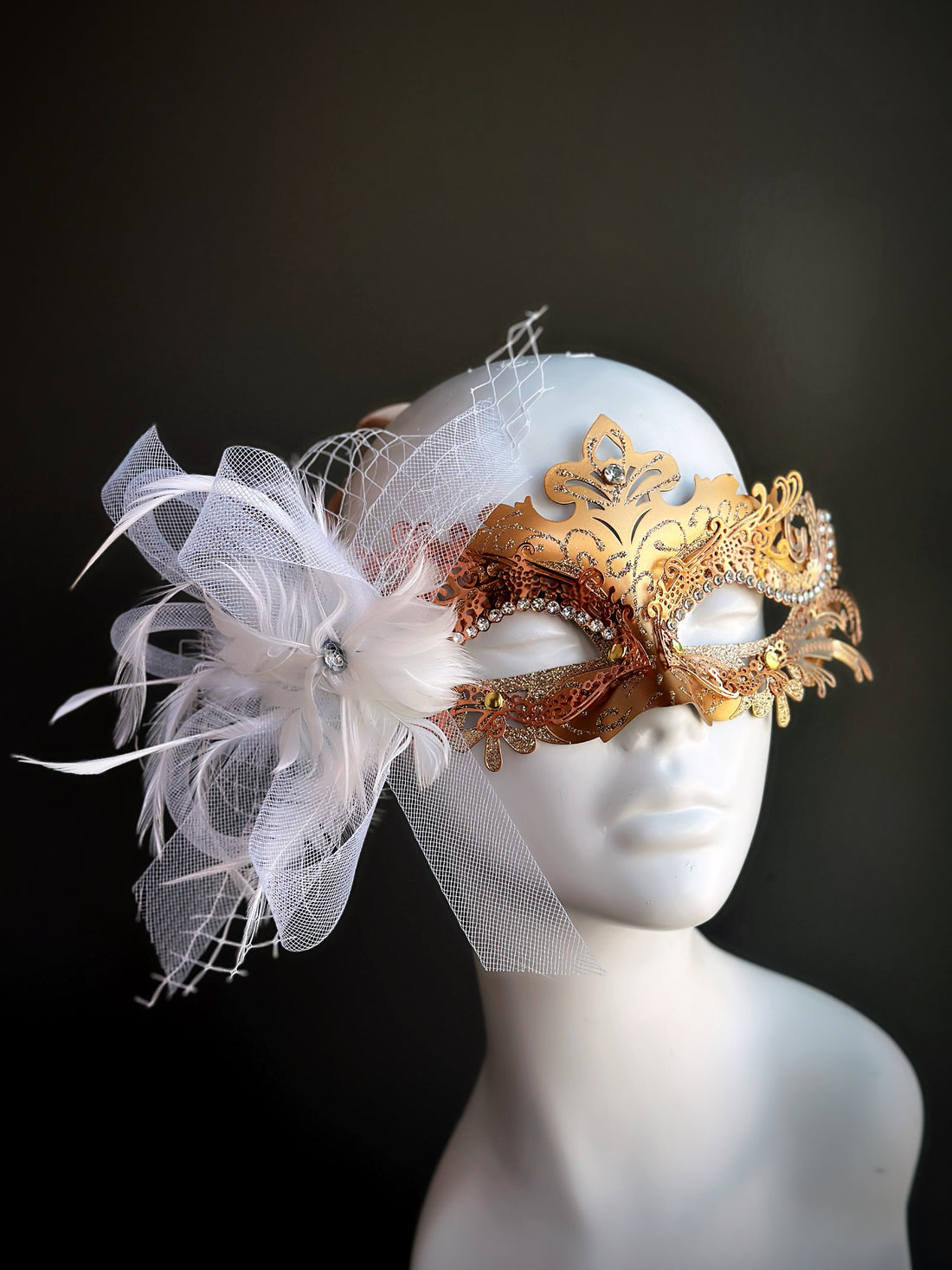 Gold filigree masquerade mask for women with white flower, feathers, and tulle detail.