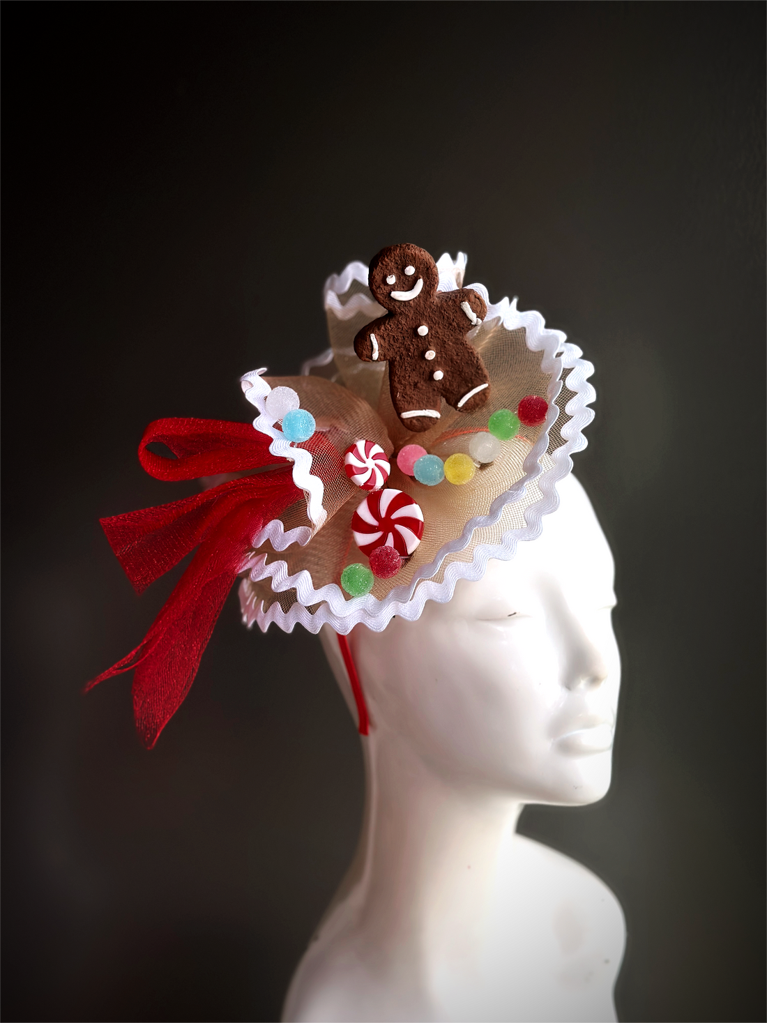 A delightful fascinator featuring a smiling gingerbread man, colorful candy accents, and festive red ribbon. Perfect for holiday parties and celebrations.