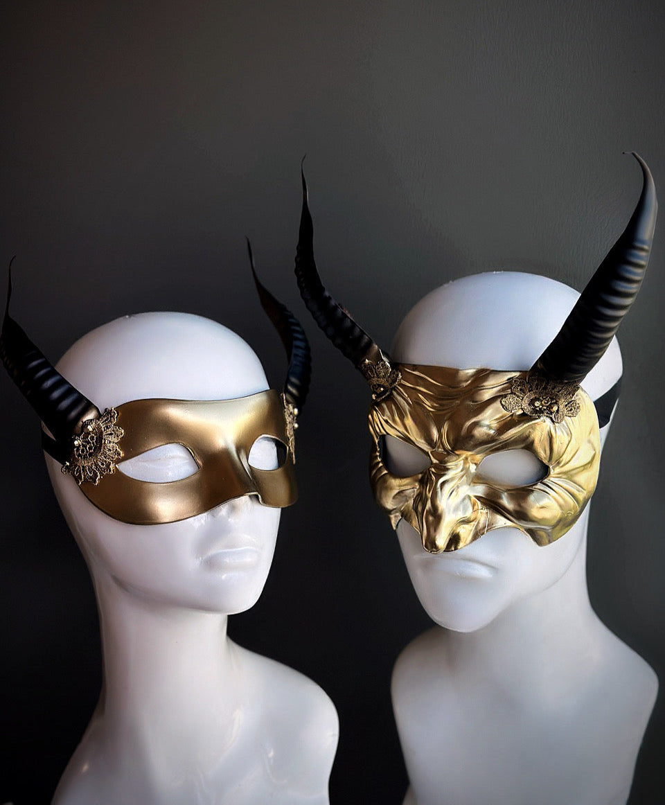 Gold horned couples mask set with a sleek half-mask for her and a sculpted demonic mask for him, featuring black curved horns and filigree details.


