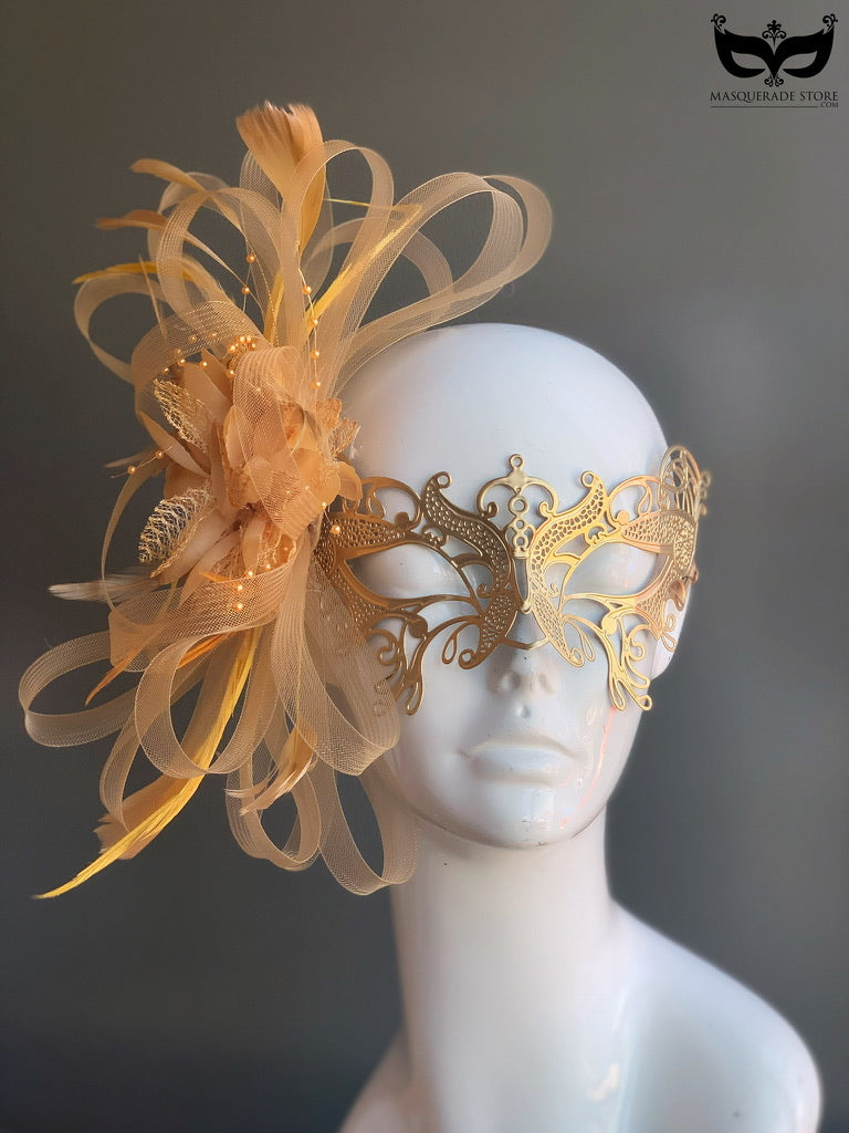 Gold metal mask featuring intricate filigree, soft tulle accents, and elegant feather details.