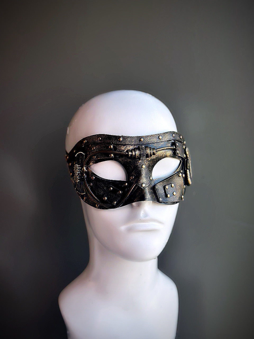 Gold steampunk masquerade mask with industrial details and riveted accents displayed on a mannequin head.