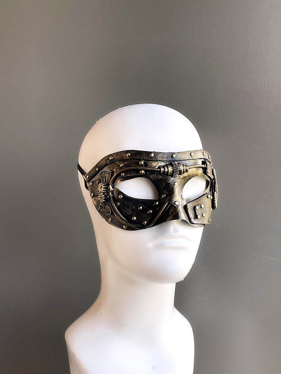 Gold steampunk masquerade mask with rivet and gear details displayed on a mannequin head.
