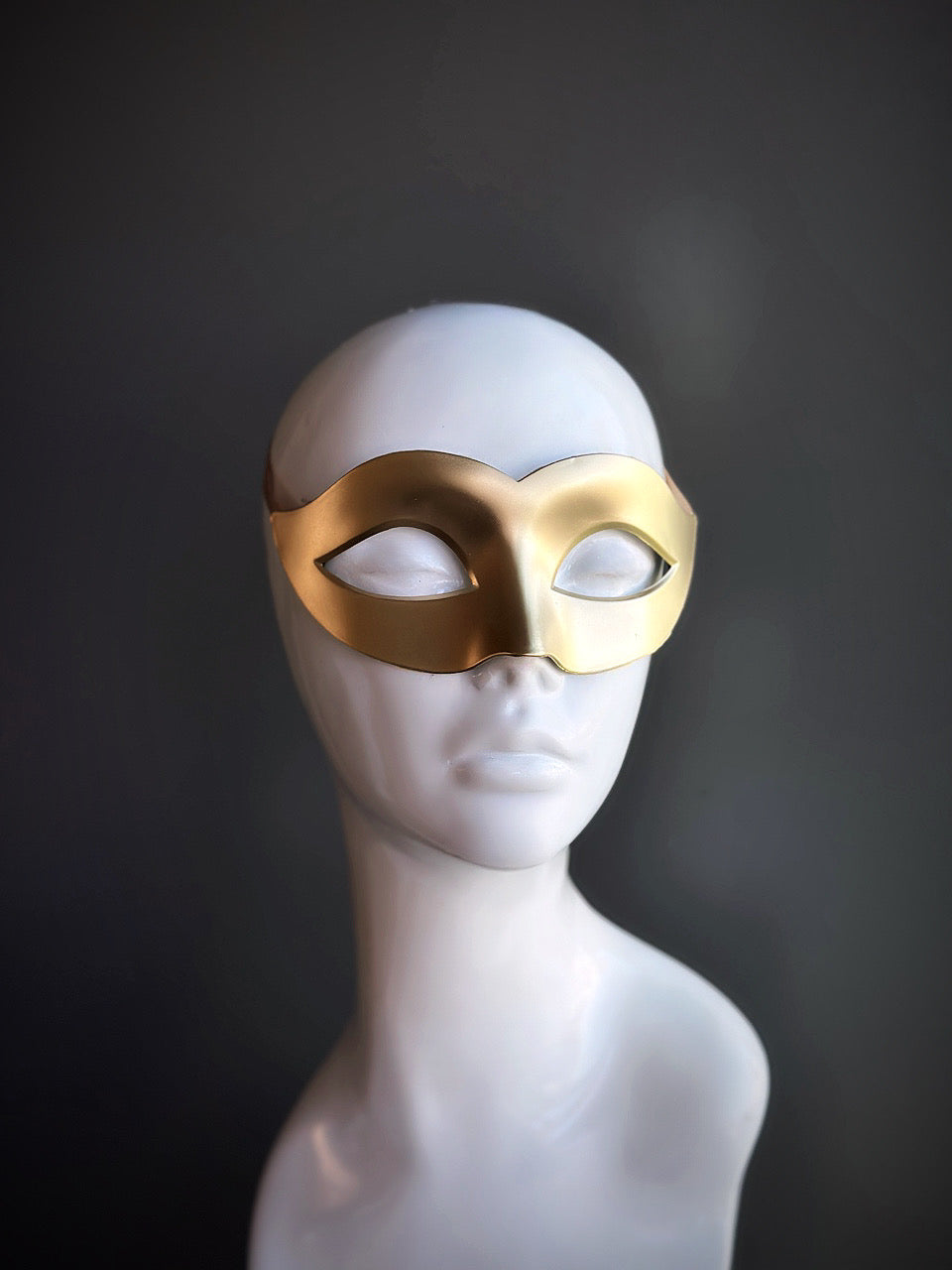 Sleek gold Venetian eye mask with a minimalist design displayed on a mannequin.

