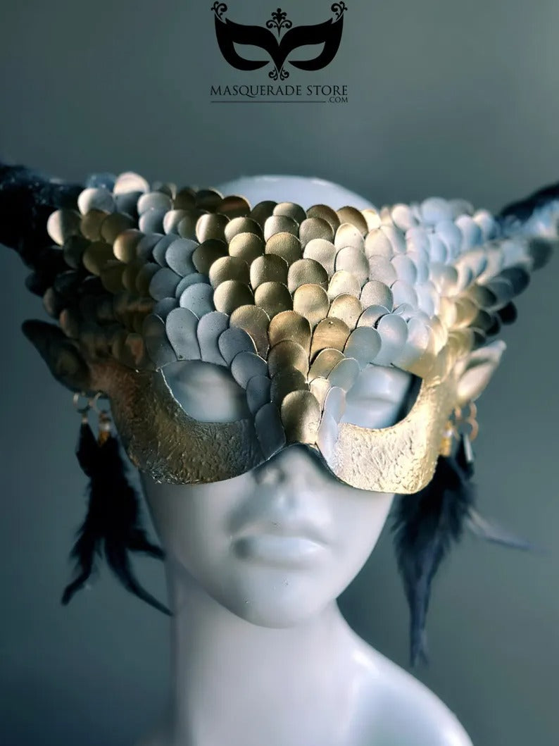 Fantasy dragon horn masquerade mask in gold with scales, black horns, and feather accents, designed as a dramatic headdress.