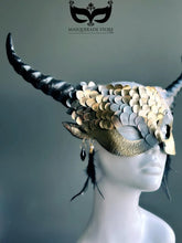 Fantasy dragon horn masquerade mask in gold with scales, black horns, and feather accents, designed as a dramatic headdress.