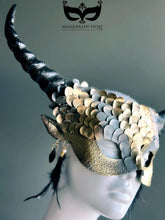 Fantasy dragon horn masquerade mask in gold with scales, black horns, and feather accents, designed as a dramatic headdress.