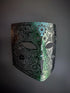 Laser-cut metal mask with an ombre effect, fading from emerald green in the center to black on the sides, featuring intricate filigree detailing.

