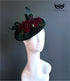 Green velvet fascinator hat with red floral accents.